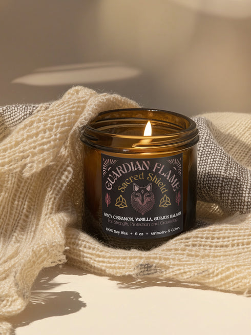 Amber glass jar with Guardian Flame label featuring a metallic wolf and flame motifs in pink and gold. Spicy cinnamon, vanilla, and gurjun balsam candle. 9 oz soy candle by Grimoire & Goblet.